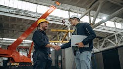 Two male workers in a factory shaking hands. Two male workers in a factory shaking hands.