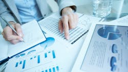Businessman at desk examining graphic representations of data — tables and charts — on printed documents and a tablet. Businessman at desk examining graphic representations of data — tables and charts — on printed documents and a tablet.