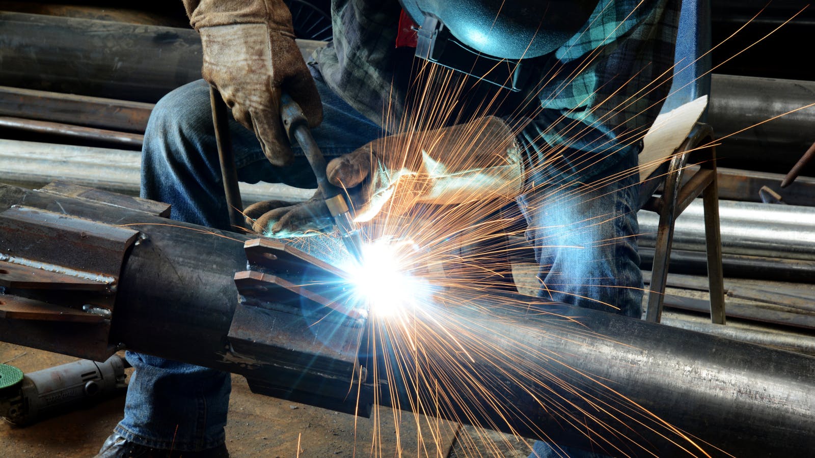 A figure in a welding mask welds, sending a spray of sparks into the air.