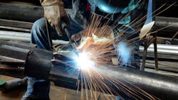 A figure in a welding mask welds, sending a spray of sparks into the air. A figure in a welding mask welds, sending a spray of sparks into the air.