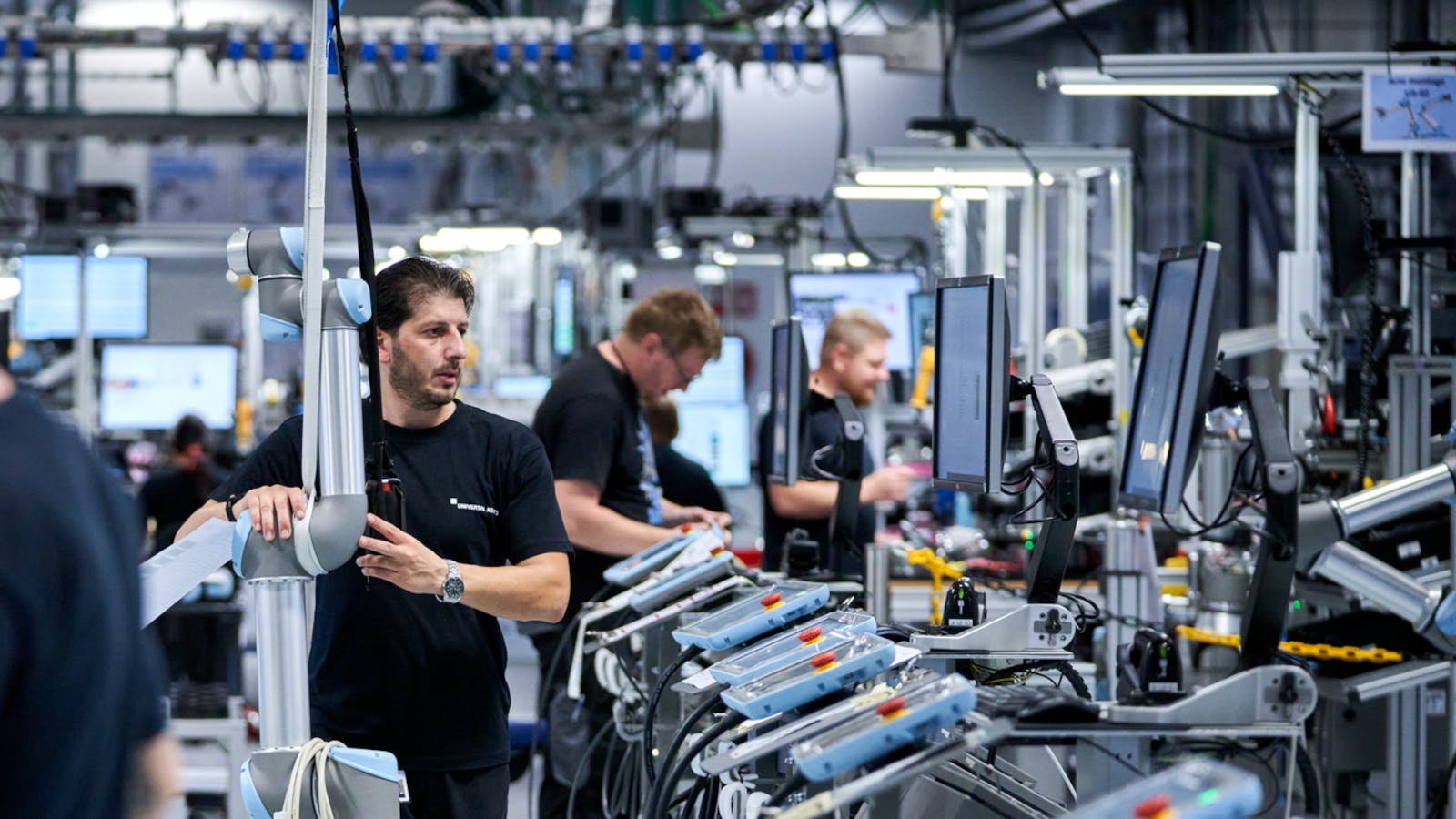 A factory worker carries part of a robot arm across the shop floor.