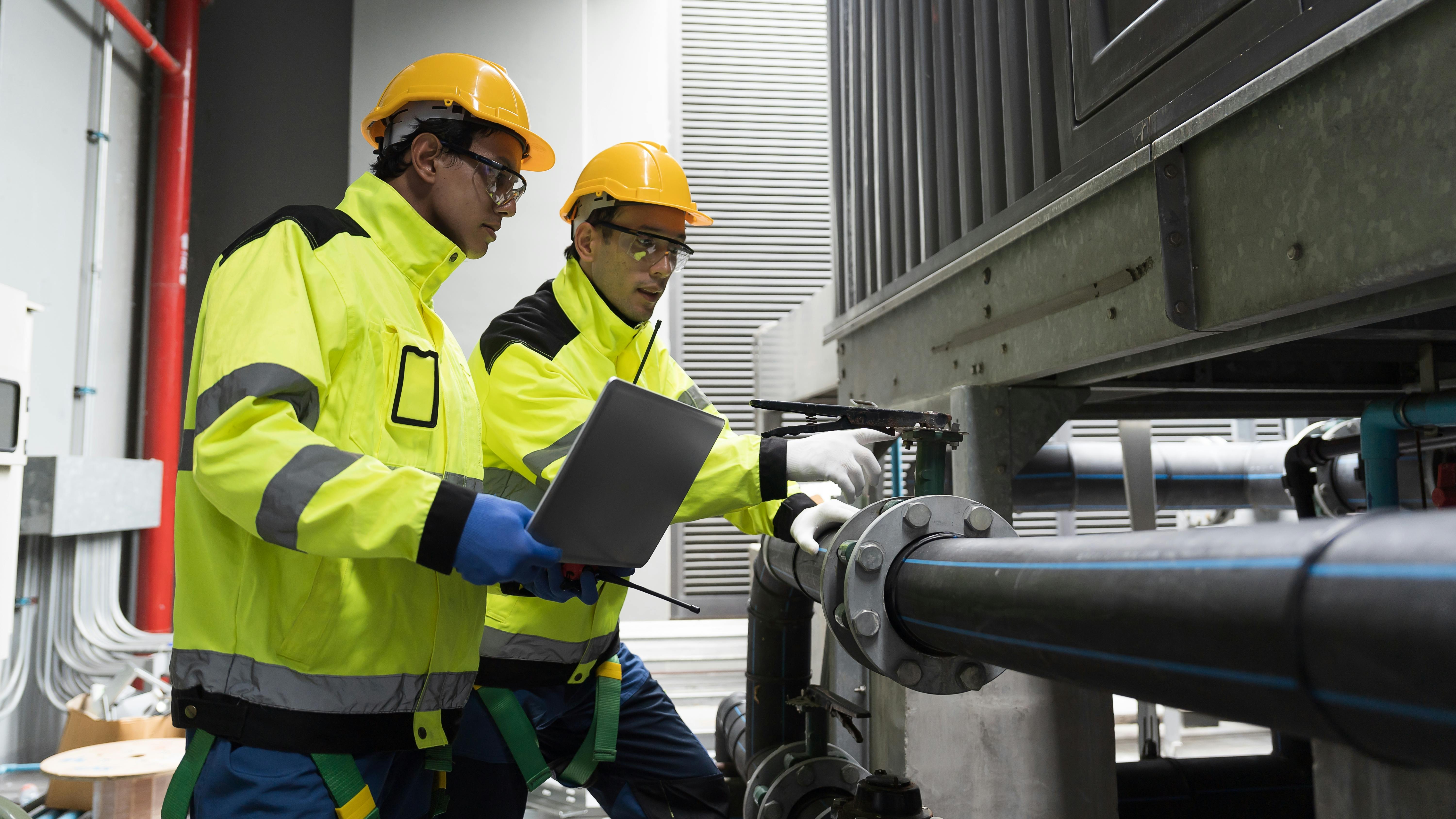 Two technicians repair a pipe in a factory