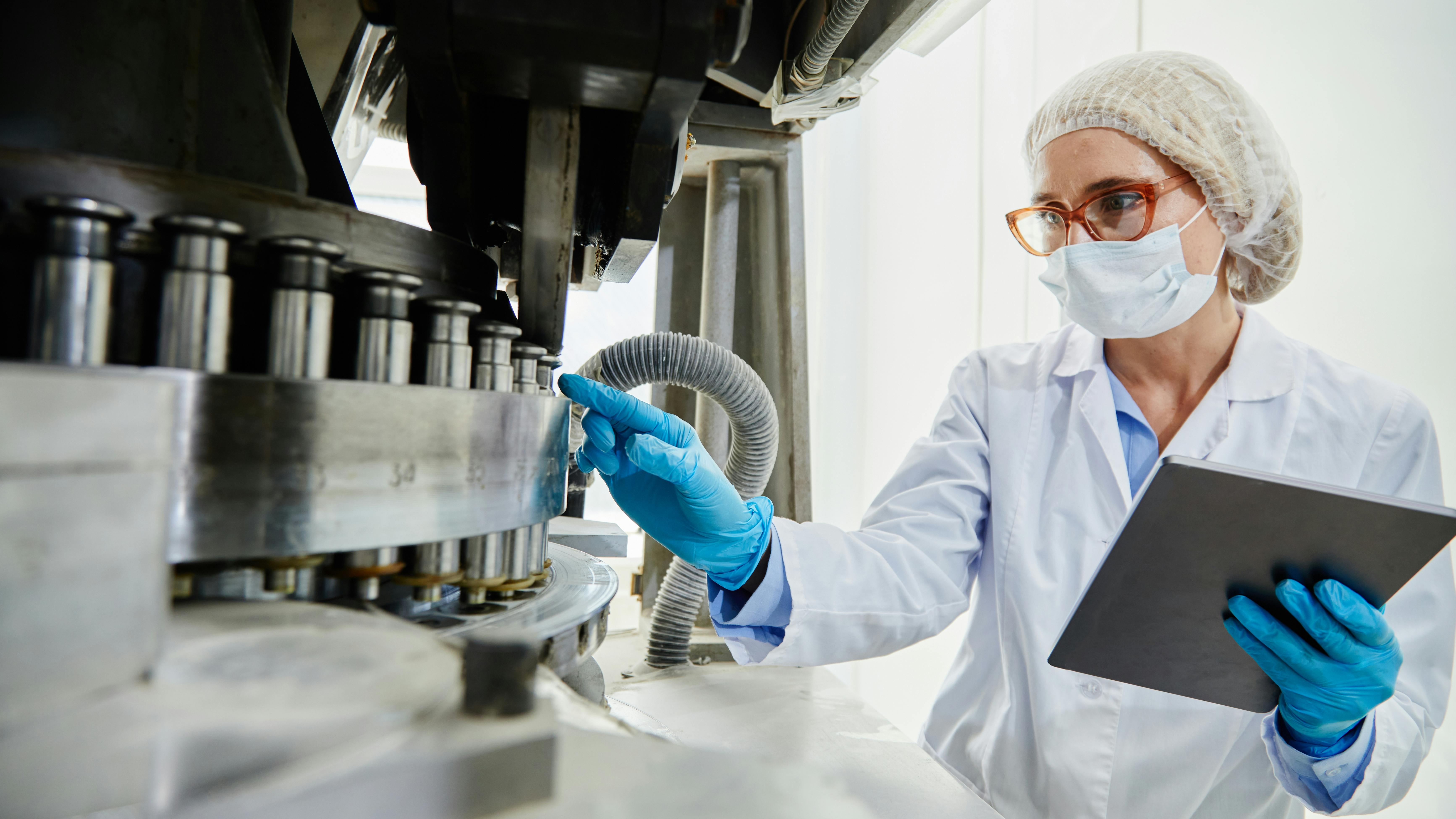 A process technician examines pharmaceutical manufacturing equipment